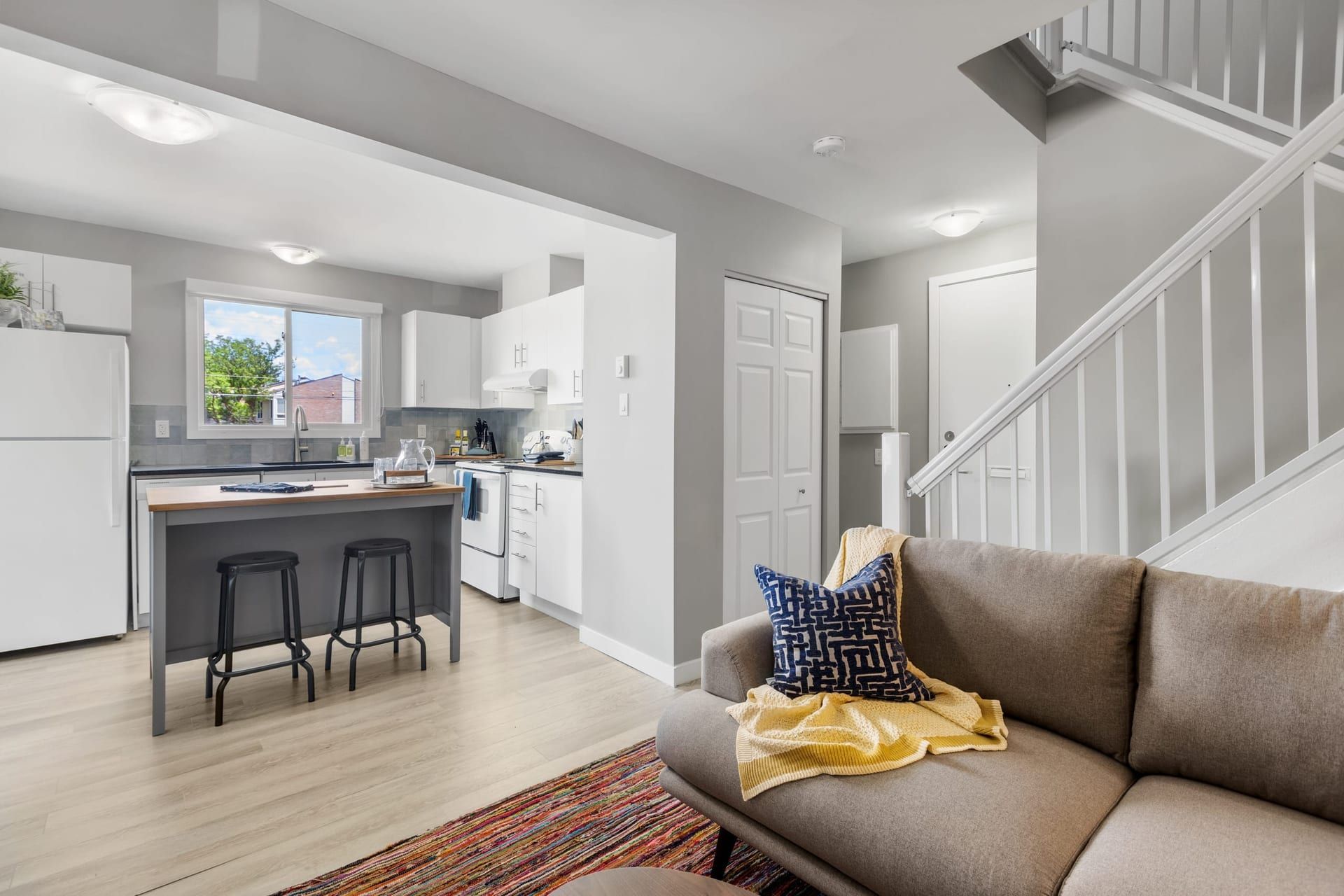 Inside a home at Woodroffe Towns: an open kitchen with a wooden island and stools, opening onto a living room, with a staircase to the upper floor.
